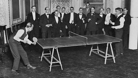Partido de tenis de mesa en un salón rodeado de espectadores
